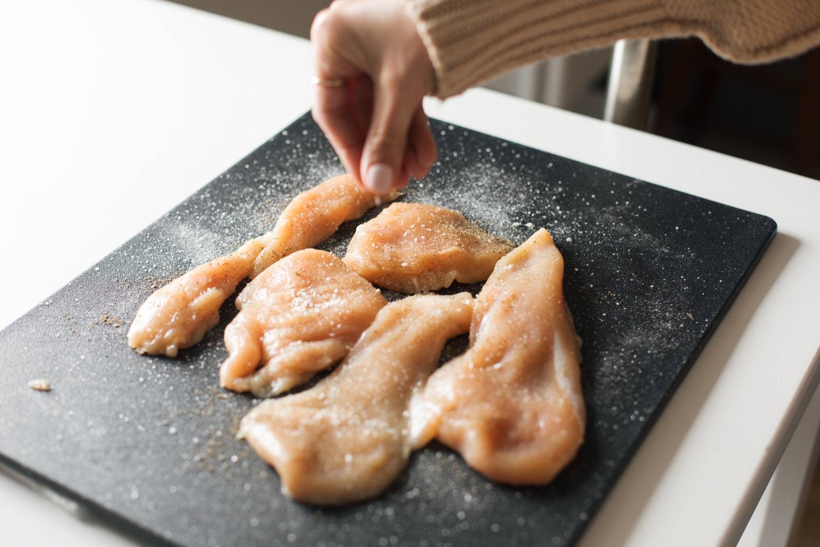 Sprinkling salt and pepper on chicken.