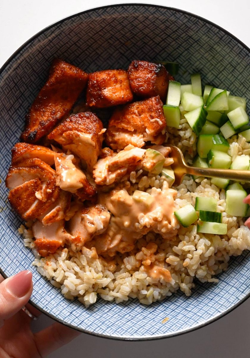 Air fryer salmon in a bowl with rice, cucumber, and sauce.